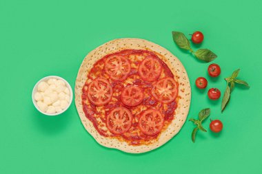 Lezzetli pizza ve yeşil arka planda malzemeler.