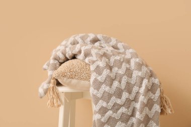 Yastıklı tabure ve bej duvarın yanında rahat battaniye