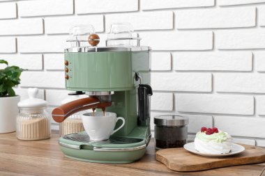 Modern coffee machine with cup of hot espresso and cake on table in kitchen