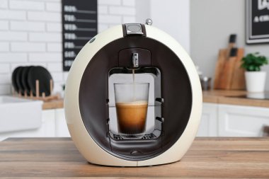 Modern coffee machine with glass of hot americano on table in kitchen