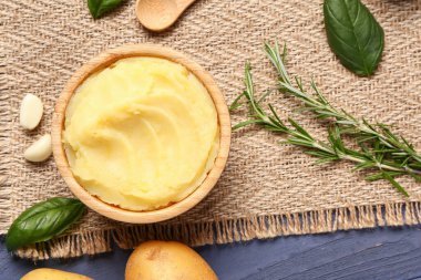 Mavi ahşap arka planda biberiye ve fesleğenli bir kase lezzetli patates püresi.