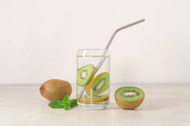 Beyaz zemin üzerinde kivi ve nane ile doldurulmuş su bardağı