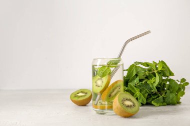 Beyaz zemin üzerinde kivi ve nane ile doldurulmuş su bardağı