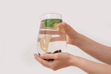 Beyaz arka planda böğürtlen ve limon dolu bir sürahi su tutan kadın.