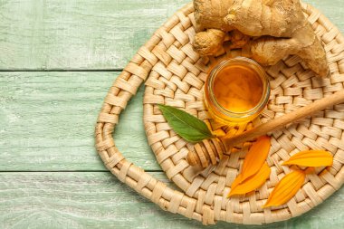 Zencefilli bal kavanozu ve yeşil ahşap arka planda taç yaprakları.