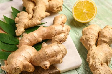 Taze zencefil kökleri, yaprakları ve yeşil ahşap arka planda yarım limon.