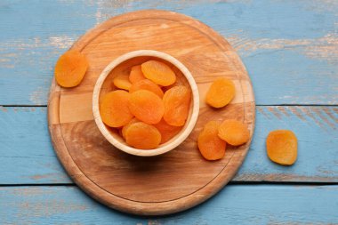 Mavi ahşap arka planda lezzetli kurutulmuş kayısı kasesi.