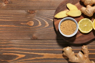 Tahta zemin üzerinde taze zencefil kökleri, limon ve bir kase kurutulmuş toz olan tahta.