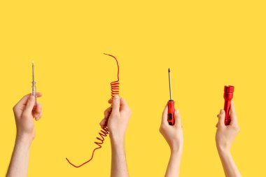 Electrician hands with tools and wire on yellow background