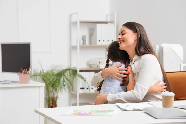 Working mother with her little daughter hugging in office
