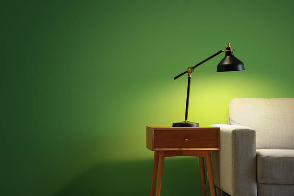 Glowing lamp on table and sofa near green wall in living room
