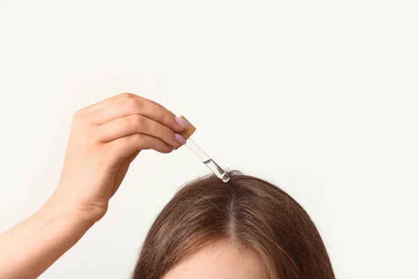 stock image Young woman using cosmetic oil for hair treatment on light background, closeup