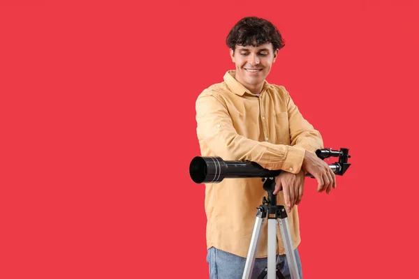 赤い背景に望遠鏡を持っている若い男 — ストック写真