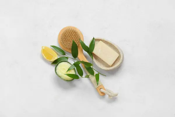 Bowl of lemon body scrub with massage brush and soap on white background