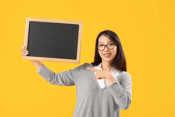 Vrouwelijke Aziatische Leraar Wijzend Schoolbord Gele Achtergrond — Stockfoto
