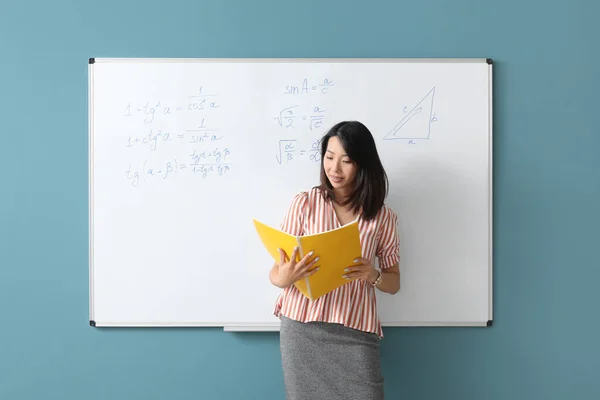 教室のフリップボード近くのノートを持つアジアの数学の教師 — ストック写真