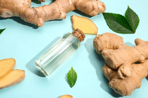 Bottle of ginger cosmetic oil and leaves on blue background