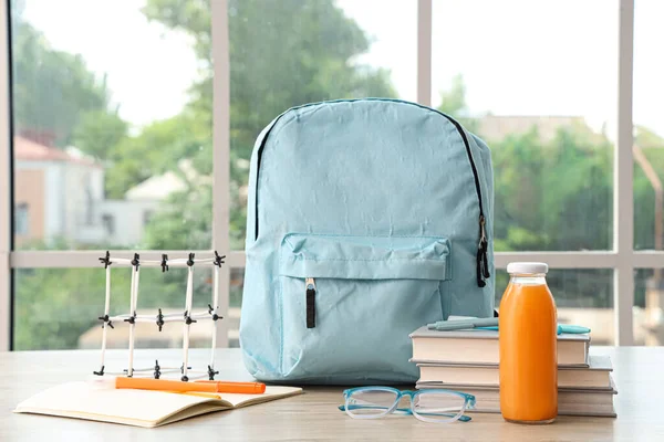 教室窗户边的木制桌子上 蓝色校服背包 装有文具 分子模型和果汁瓶 — 图库照片