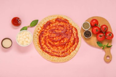 Domates soslu pizza hamuru ve pembe arka planda malzemeler.