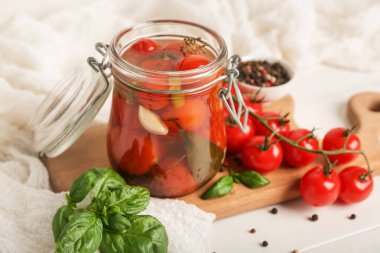 Jar with canned tomatoes and basil on white wooden table
