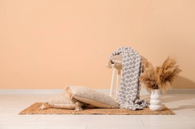 Yastıklar, battaniye ve vazo, bej duvarın yanında otlar.