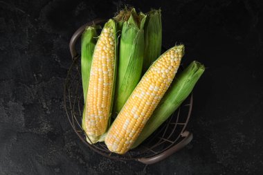 Siyah arka planda taze mısır koçanları olan sepet.