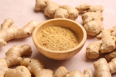 Taze zencefil kökleri ve pembe zemin üzerinde kurumuş toz bulunan ahşap kase.