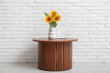 Güzel ayçiçekleri olan vazo ve boş çerçeve odanın duvarının yanındaki masada.