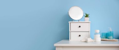 Mavi duvarın yanındaki çekmeceli, aynalı ve çiçekli banyo aksesuarları. Tasarım için pankart