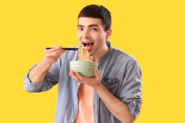 Young man eating Chinese noodles on yellow background