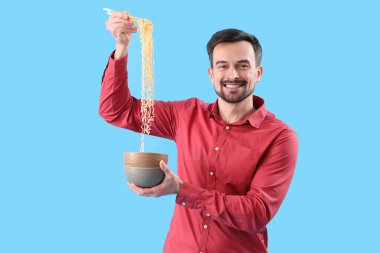 Mavi arka planda bir kase Çin eriştesi olan yakışıklı bir adam.