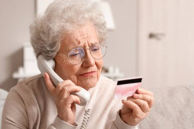 Kredi kartıyla evde telefonla konuşan yaşlı bir kadın, yakın plan.