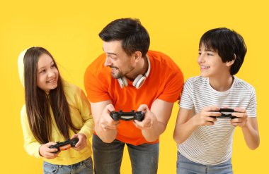 Baba ve küçük çocukları sarı arka planda video oyunu oynuyorlar.