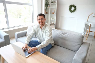 Evde dizüstü bilgisayar kullanan şık gözlüklü yakışıklı bir adam.