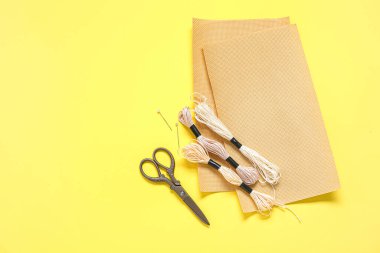 Sarı arka planda makaslı tuval, küflü iplikler ve iğneler.