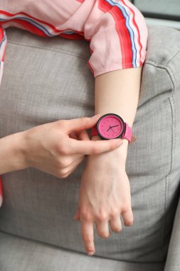 Kanepede oturan ve odada şık kol saatine bakan genç bir kadın.