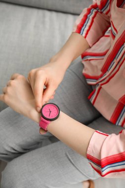 Kanepede oturan ve odada şık kol saatine bakan genç bir kadın.