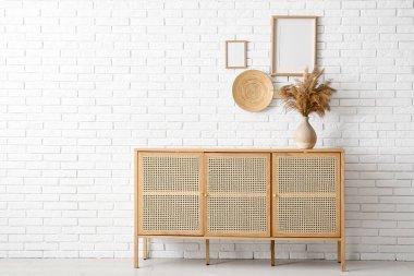 Çimenli modern çekmeceler ve odadaki açık tuğlalı duvarda asılı boş resimler.