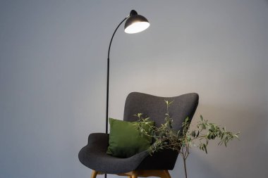 Parlayan lamba, gri koltuk, yastıklı ve gri duvarın yanında saksı bitkisi.