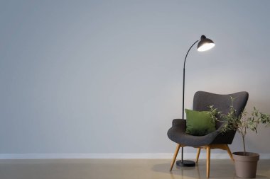 Parlayan lamba, gri koltuk, yastıklı ve gri duvarın yanında saksı bitkisi.