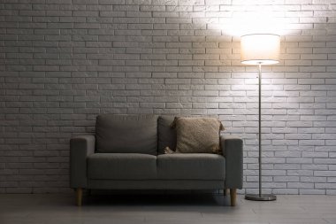 Gri kanepede, karanlık odada parlayan lamba.