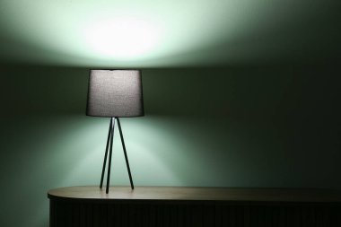 Karanlık odadaki ahşap masada parlayan lamba.