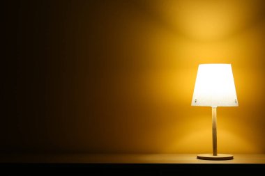 Karanlık odadaki ahşap masada parlayan lamba.