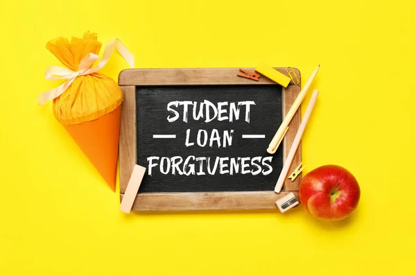 stock image Chalkboard with text STUDENT LOAN FORGIVENESS, apple and school cone on yellow background