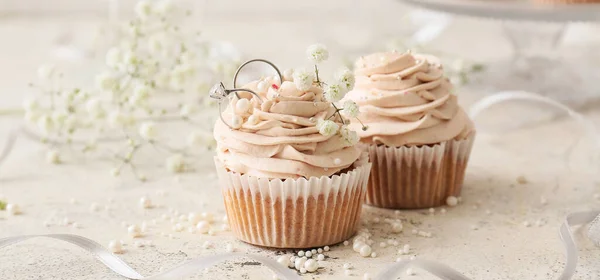 Beautiful cupcakes with wedding rings on light background