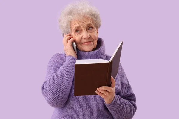 Mulher Sênior Com Livro Falando Por Telefone Celular Fundo Lilás — Fotografia de Stock