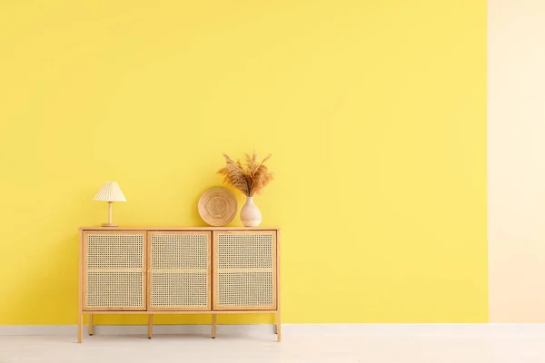 stock image Modern chest of drawers with pampas grass, lamp and plate near orange wall in room