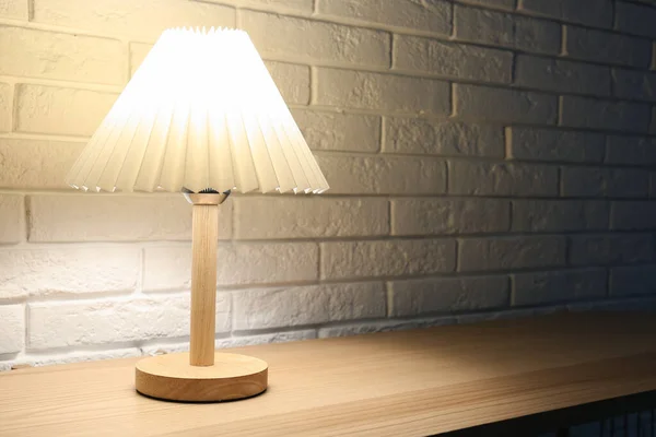 Lampa Świecąca Drewnianym Stole Pobliżu Ściany Białej Cegły Ciemnym Pomieszczeniu — Zdjęcie stockowe