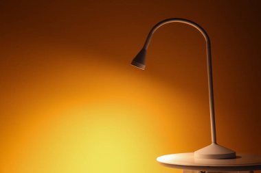 Karanlık odada, turuncu duvarın yanındaki masada parlayan lamba.