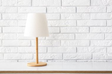 Beyaz tuğla duvarın yanındaki çekmecelerin üzerindeki masa lambası.